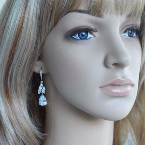 May include: A pair of silver teardrop earrings with clear crystal accents. The earrings are dangling from the earlobes of a mannequin with blonde hair.
