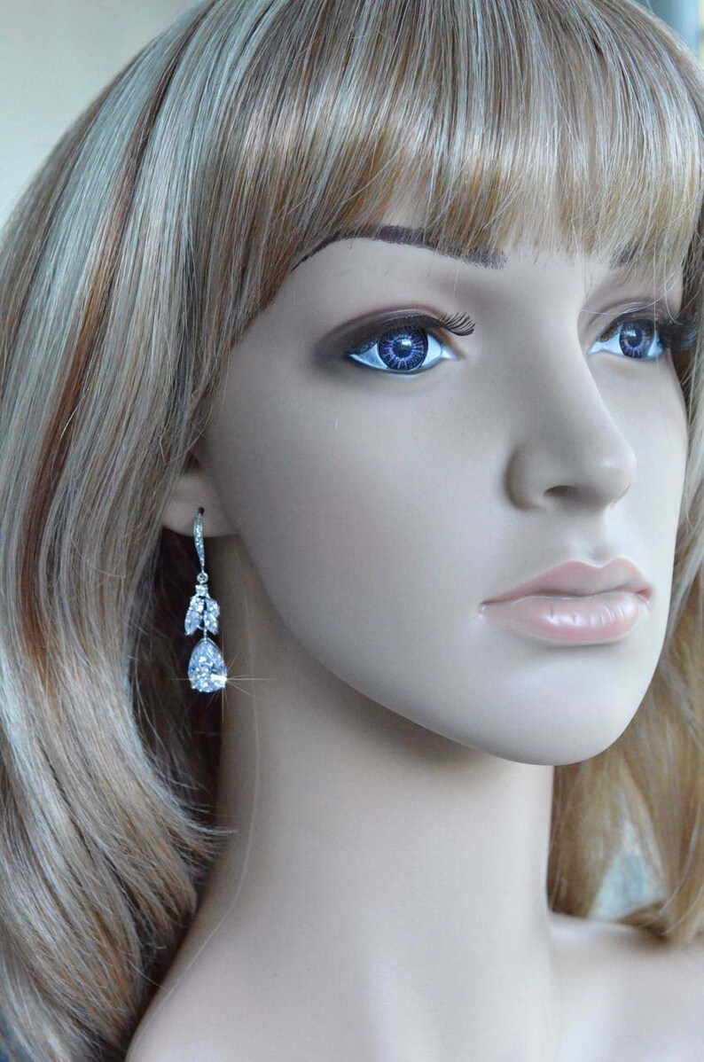 May include: A pair of silver teardrop earrings with clear crystal accents. The earrings are dangling from the earlobes of a mannequin with blonde hair.