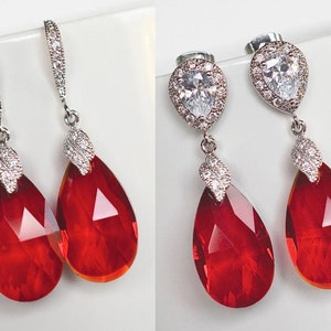 May include: A pair of red teardrop-shaped crystal earrings with silver settings and clear crystal accents.