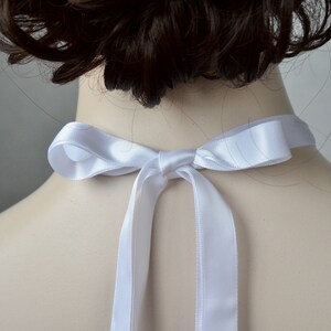 May include: White satin ribbon tied in a bow around the neck. The ribbon is tied in a simple knot with two long tails.