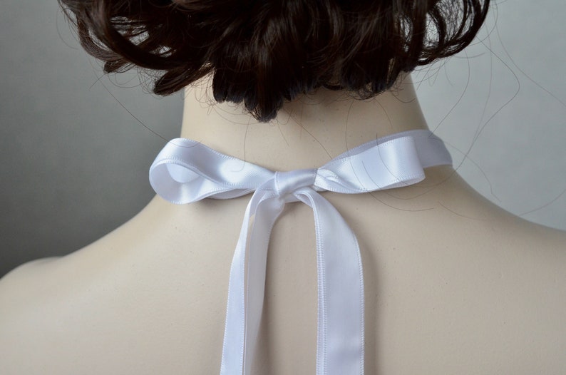 May include: White satin ribbon tied in a bow around the neck. The ribbon is tied in a simple knot with two long tails.