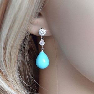 May include: Silver dangle earrings with a turquoise teardrop-shaped stone and clear cubic zirconia accents.