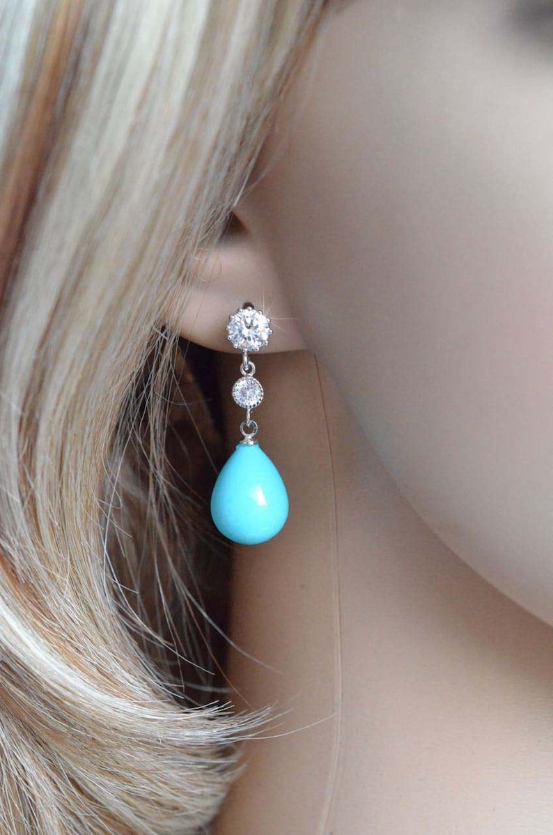May include: Silver dangle earrings with a turquoise teardrop-shaped stone and clear cubic zirconia accents.