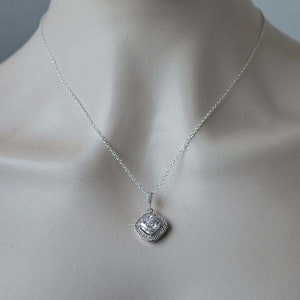 May include: A silver necklace with a square-shaped pendant featuring a large clear cubic zirconia stone surrounded by smaller clear stones.