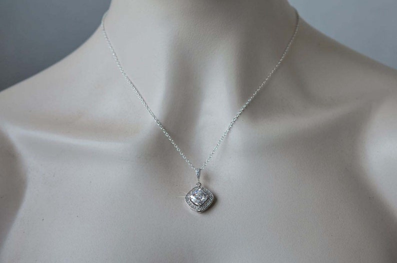 May include: A silver necklace with a square-shaped pendant featuring a large clear cubic zirconia stone surrounded by smaller clear stones.