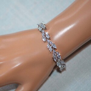 May include: A silver bracelet with a leaf design featuring clear cubic zirconia stones.