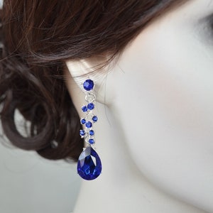 May include: A pair of dangle earrings featuring a teardrop-shaped blue crystal and smaller blue crystals arranged in a cluster.