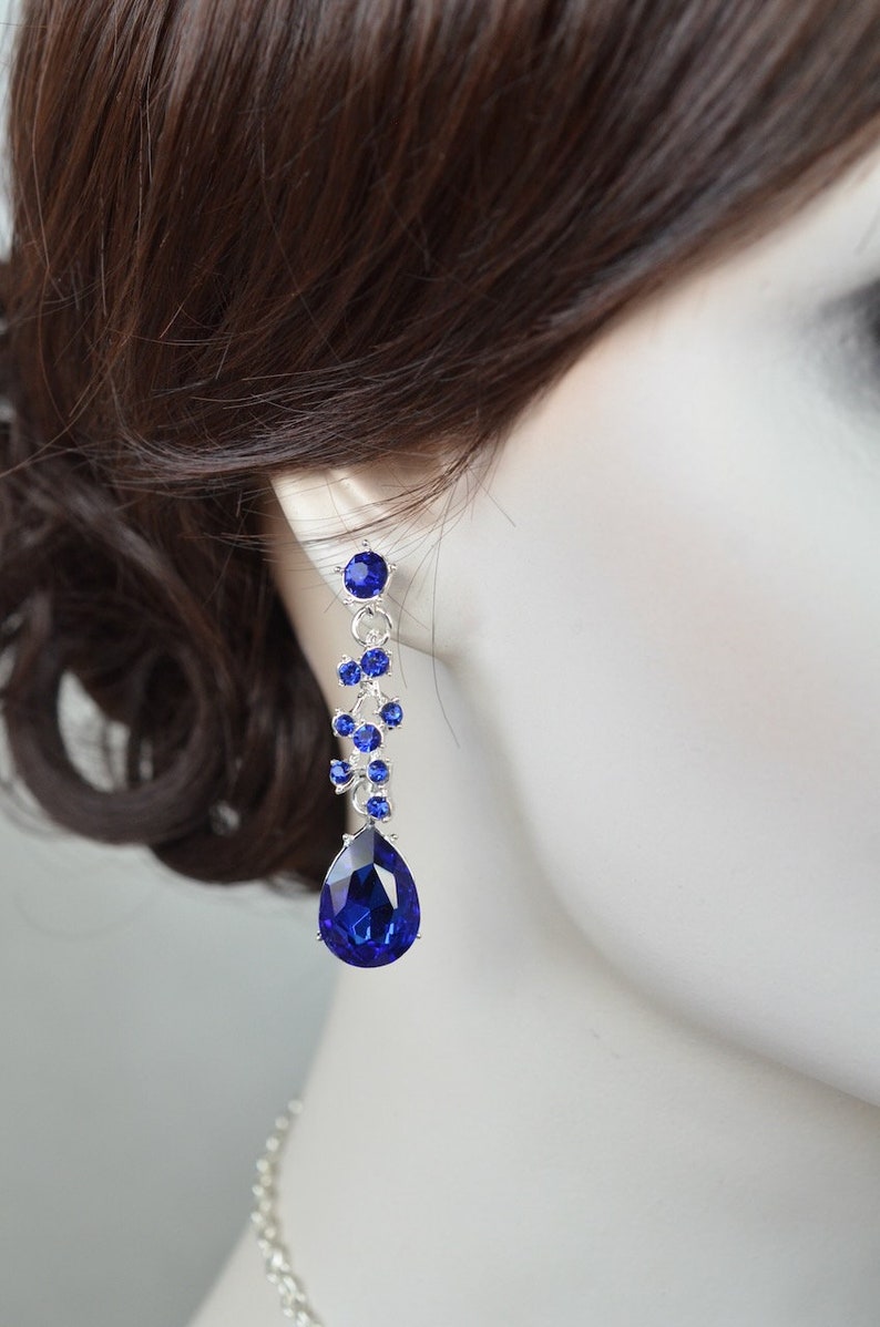 May include: A pair of dangle earrings featuring a teardrop-shaped blue crystal and smaller blue crystals arranged in a cluster.