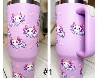 May include: A purple stainless steel travel mug with a handle. The mug features a repeating pattern of cartoon axolotls with rainbow accents. The mug is labeled with the number "#1".