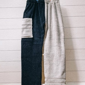 Könnte beinhalten: Zweifarbige Jogginghose, marineblau auf der einen und hellgrau auf der anderen Seite, hängt an einer Holzleiter. Die marineblaue Seite hat eine hellgraue Tasche. Die Hose ist aus einem weichen, saugfähigen Material.