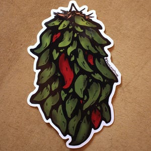 Puede incluir: Una pegatina troquelada que muestra un manojo de chiles verdes colgantes con algunos chiles rojos intercalados entre el follaje. La ilustración incluye una pequeña firma de texto negro en el lado derecho que dice ShareLittleThings.