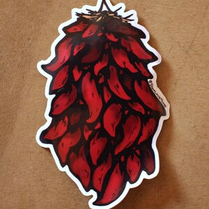 Puede incluir: Una pegatina troquelada con una ilustración colorida de una ristra de chiles rojos. El racimo de chiles está representado en tonos de rojo brillante y oscuro con contornos negros. El texto @ShareLittleThings está impreso en pequeñas letras negras a la derecha.