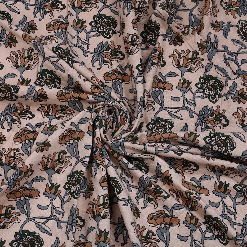 May include: A close-up of a beige fabric with a floral print. The flowers are in shades of brown, green, and blue. The fabric is soft and has a smooth texture.