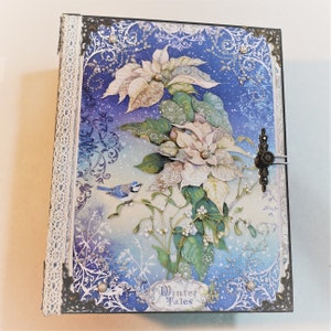 May include: A blue and white scrapbook with a winter theme. The cover features a poinsettia flower, a bluebird, and the text "Winter Tales".