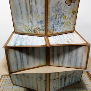 以下が含まれることがあります： 素朴でヴィンテージな雰囲気の多層紙工芸品。各層は、蝶の付いた花柄、木目柄、市松模様など、異なるデザインが施されています。この工芸品は茶色と白の紙で作られています。
