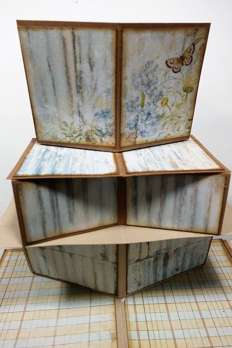 以下が含まれることがあります： 素朴でヴィンテージな雰囲気の多層紙工芸品。各層は、蝶の付いた花柄、木目柄、市松模様など、異なるデザインが施されています。この工芸品は茶色と白の紙で作られています。