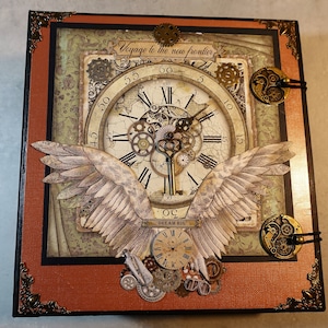 May include: A brown, leather-bound scrapbook with a steampunk theme. The cover features a large clock face with gears, wings, and the text "Voyage to the new frontier".