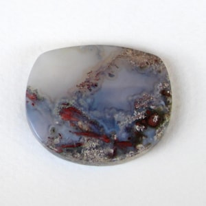 May include: A polished, square-shaped gemstone with rounded corners. The stone features a blend of white, blue, and red hues, with intricate patterns resembling a landscape. The surface has a smooth, glossy finish, highlighting the natural variations in color and texture.