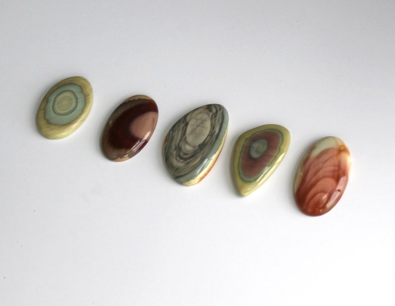 May include: Five polished oval-shaped stones with different patterns and colors, including green, brown, red, and white.