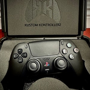 May include: A black PlayStation 5 controller with custom buttons and a Kustom Kontrollerz logo on the case.