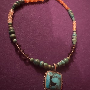 Peut inclure: Un collier avec un pendentif en pierre turquoise et un cadre argenté. Le collier est composé de perles turquoise, orange et transparentes.