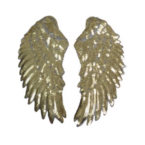 Könnte beinhalten: Ein Paar goldene Flügel mit Pailletten. Die Flügel bestehen aus einem durchsichtigen Stoff, auf den goldene Pailletten genäht sind. Die Flügel sind etwa 25 cm hoch und 15 cm breit.