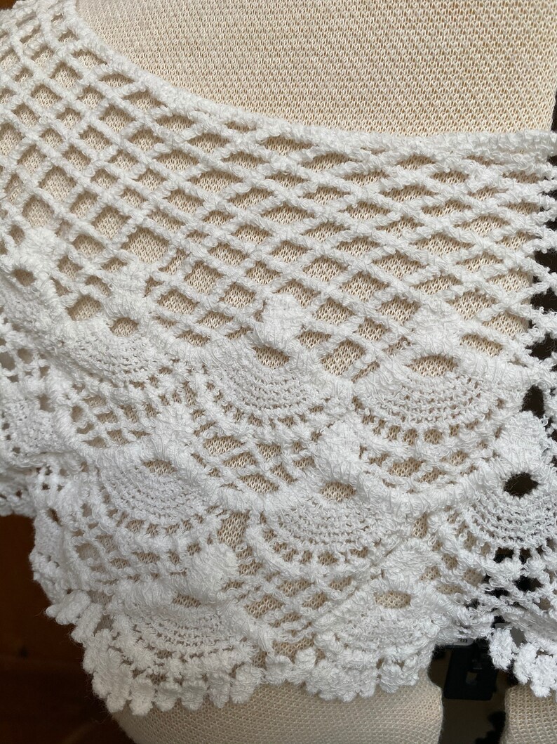 May include: White crochet lace trim with a delicate, intricate pattern. The lace has a soft, fluffy texture and a scalloped edge.
