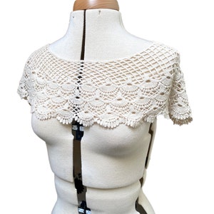 May include: A white crocheted collar with a scalloped edge. The collar is displayed on a white dress form.