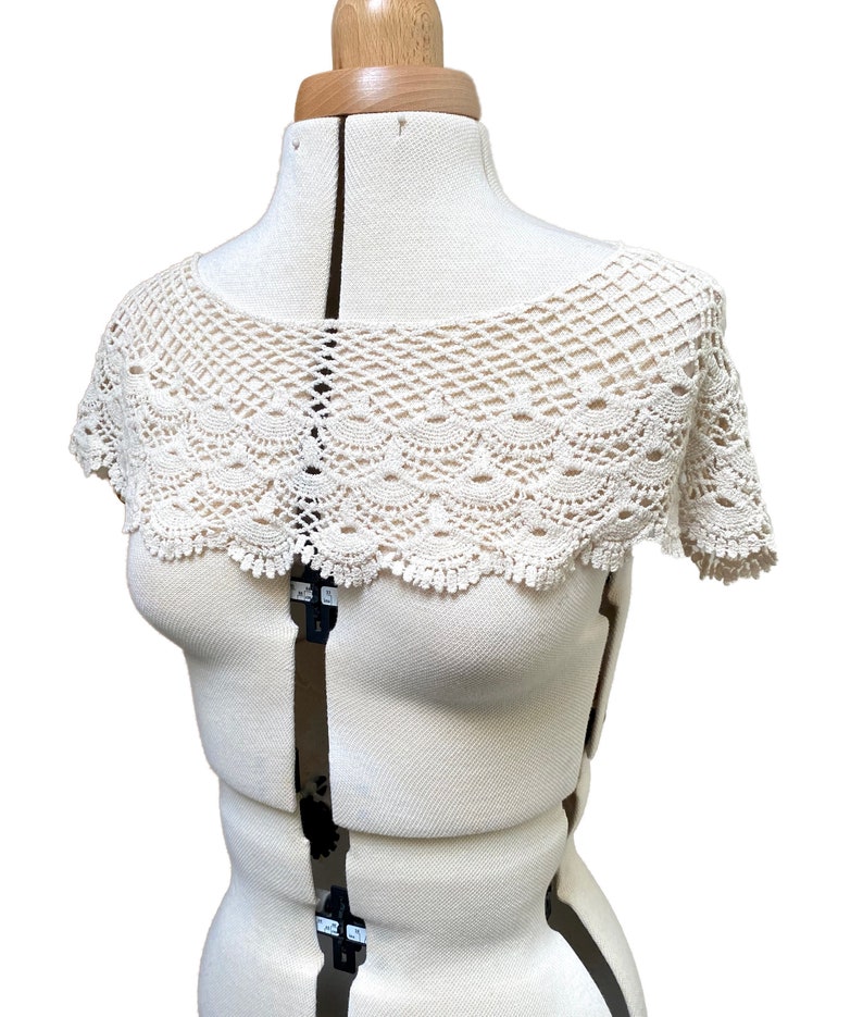 May include: A white crocheted collar with a scalloped edge. The collar is displayed on a white dress form.
