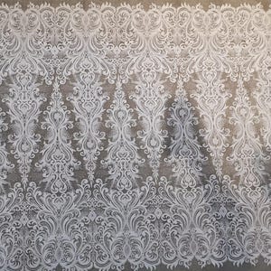 Puede incluir: Tela de encaje blanco con un intrincado patr&oacute;n floral sim&eacute;trico. El dise&ntilde;o presenta vides, hojas y detalles ornamentados sobre un fondo neutro. Adecuado para diversos proyectos de artesan&iacute;a y dise&ntilde;o.