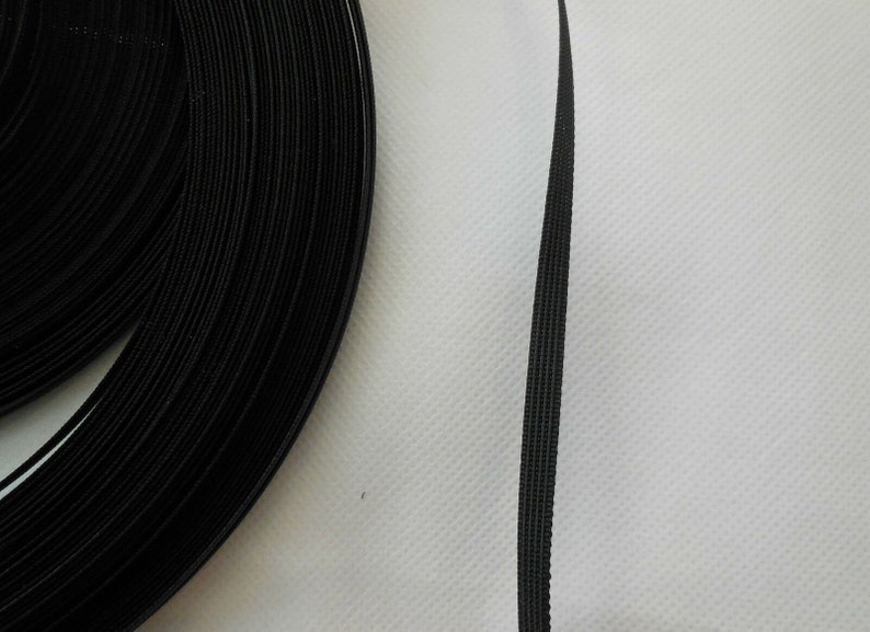 Puede incluir: Un rollo de cinta de gancho y bucle negro, tambi&eacute;n conocida como Velcro, se muestra sobre una superficie blanca. La cinta est&aacute; enrollada y una sola tira se extiende para mostrar la textura del material.