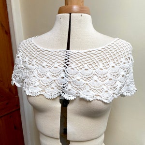 May include: White crocheted lace collar with a scalloped edge. The collar is displayed on a white dress form.