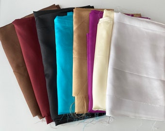 May include: A collection of eight fabric swatches in various colors, including brown, burgundy, black, turquoise, beige, purple, cream, and white. The fabrics are arranged in a fan shape, with the brown fabric at the bottom and the white fabric at the top.