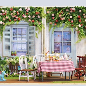 May include: A miniature dollhouse scene featuring a table set for tea with a red and white checked tablecloth. The windows and door are adorned with climbing roses and greenery. A blue rocking horse is on the grass.
