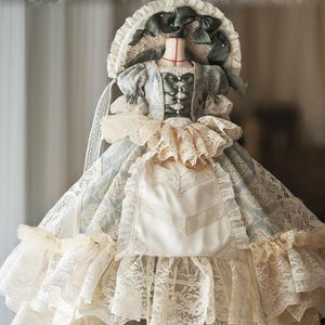 Puede incluir: Vestido de estilo vintage con un gorro, exhibido en un maniqu&iacute;. El vestido presenta un estampado floral azul claro y blanco, ribetes de encaje y una falda con volantes. El gorro est&aacute; adornado con lazos y encaje, creando una est&eacute;tica rom&aacute;ntica.
