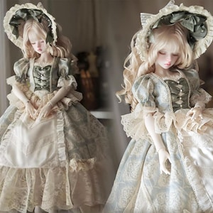 Puede incluir: Dos mu&ntilde;ecas de porcelana con vestidos de &eacute;poca. Las mu&ntilde;ecas visten vestidos azul claro y crema con detalles de encaje y cintas. Cada mu&ntilde;eca tiene pelo rubio largo y ondulado y un gorro a juego con un lazo.