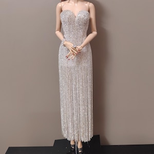 May include: A silver sequin strapless evening gown. The dress has a sweetheart neckline and a fitted bodice that flows into a column skirt. The gown is floor-length and covered in shimmering sequins, designed to reflect light and create a dazzling effect.