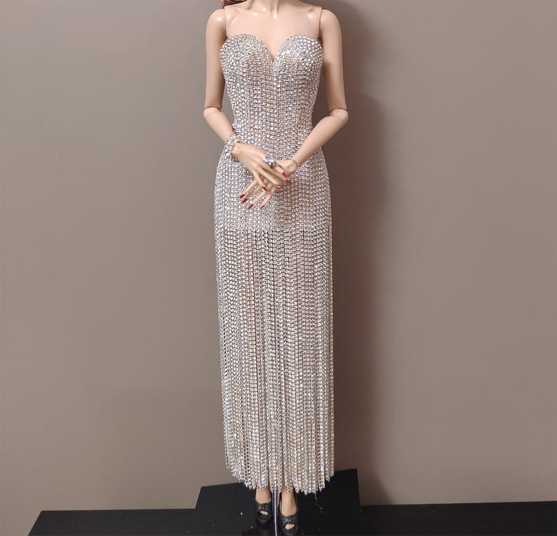 May include: A silver sequin strapless evening gown. The dress has a sweetheart neckline and a fitted bodice that flows into a column skirt. The gown is floor-length and covered in shimmering sequins, designed to reflect light and create a dazzling effect.