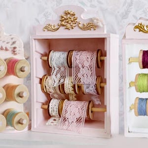 Puede incluir: Tres organizadores decorativos de madera para hilos y cintas en rosa suave y blanco. Los organizadores presentan carretes de hilo y encaje coloridos, con detalles ornamentados y detalles dorados. Los organizadores están diseñados para guardar diversos suministros de manualidades.