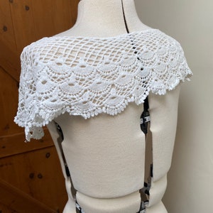 May include: White crochet lace collar with a scalloped edge. The collar is displayed on a white dress form.