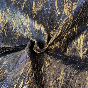 May include: Close-up of a fabric with a textured, abstract pattern. The fabric is a dark blue color with gold metallic accents.