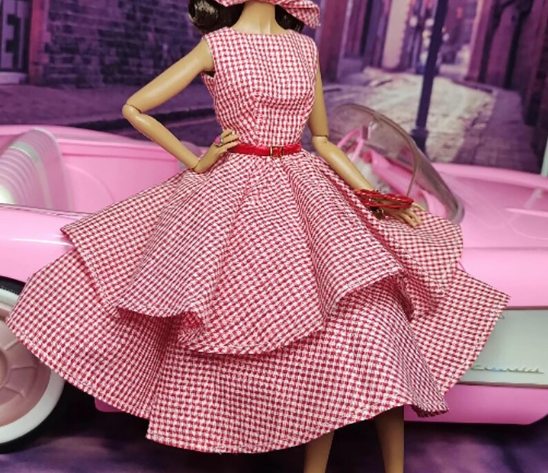 K&ouml;nnte beinhalten: Ein rot-wei&szlig; kariertes Kleid mit vollem Rock und rotem G&uuml;rtel. Das Kleid ist geschichtet und hat einen Vintage-Stil.