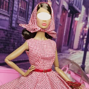 K&ouml;nnte beinhalten: Eine Puppe in einem rot-wei&szlig; karierten Kleid mit passendem Kopftuch. Die Puppe tr&auml;gt einen roten G&uuml;rtel und h&auml;lt eine kleine Handtasche.