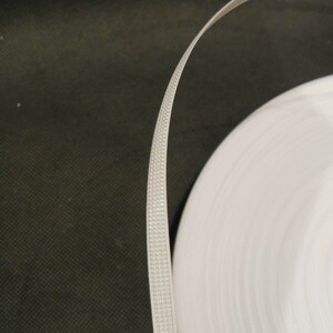 Puede incluir: Un rollo de fleje de pl&aacute;stico blanco, un tipo de material de embalaje utilizado para asegurar art&iacute;culos.
