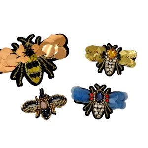 May include: Four embroidered bee patches with gold, blue, and black sequins. The bees have jeweled accents and are perfect for adding a touch of whimsy to clothing, bags, or other accessories.
