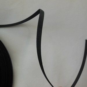 Puede incluir: Cord&oacute;n el&aacute;stico negro, enrollado en una bobina, con una longitud recta de cord&oacute;n que se extiende desde la bobina.