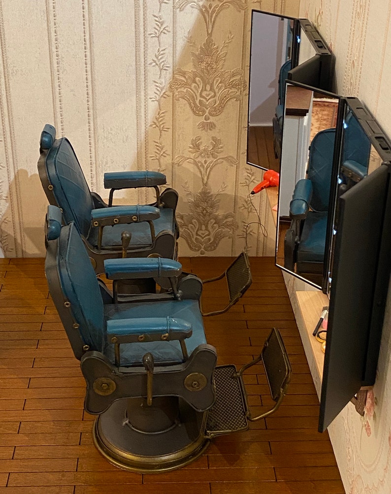 K&ouml;nnte beinhalten: Zwei Vintage-Friseurst&uuml;hle mit blauer Polsterung und Metallrahmen. Die St&uuml;hle stehen in einem Raum mit einem Spiegel und Holzboden.