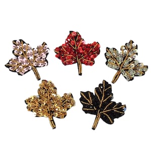 May include: Five different coloured maple leaf patches with sequins. The leaves are red, pink, gold, black and white.