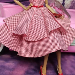 K&ouml;nnte beinhalten: Ein rot-wei&szlig; kariertes Kleid mit vollem Rock und einem roten G&uuml;rtel. Das Kleid ist geschichtet und hat einen Vintage-Stil.