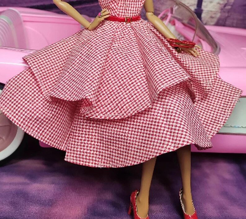 K&ouml;nnte beinhalten: Ein rot-wei&szlig; kariertes Kleid mit vollem Rock und einem roten G&uuml;rtel. Das Kleid ist geschichtet und hat einen Vintage-Stil.